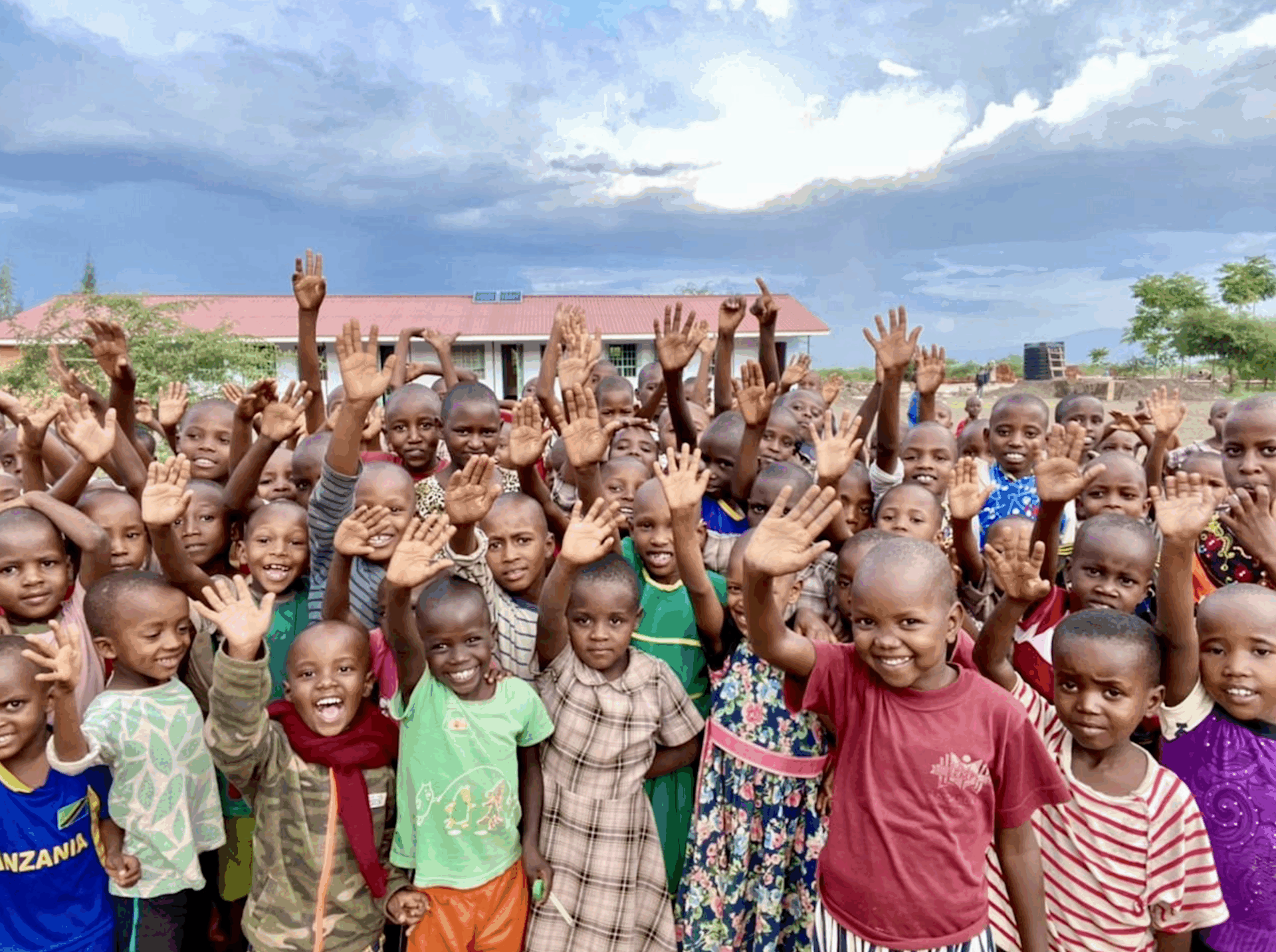 A large group of young students smiling and waving.