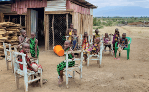 A group of children seated in ladderback chairs outside