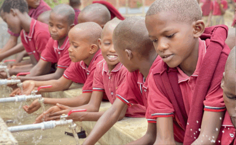 Students washing their hands at a large sink with multiple faucets